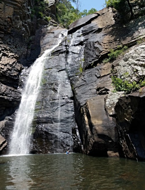 A tall waterfall cascading down rocky cliffs into a serene pool below, surrounded by lush greenery.