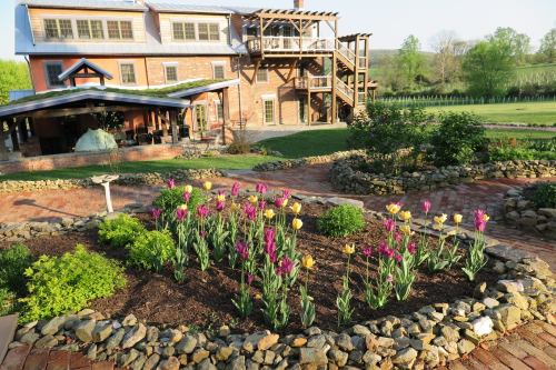 A garden with colorful tulips in front of a rustic building and green landscape, featuring stone pathways and trees.