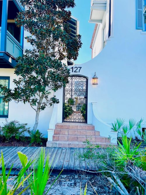 A white house entrance with a decorative gate, steps, and greenery, featuring a lantern and the number 127.