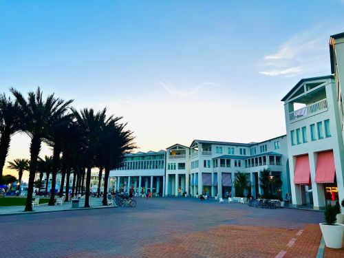 A scenic view of a coastal promenade lined with palm trees and modern buildings under a clear blue sky.