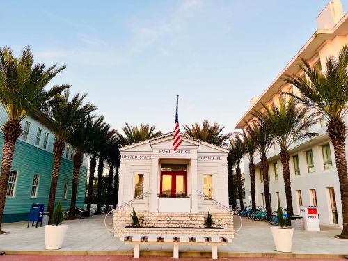 A small white post office building surrounded by palm trees, with an American flag and nearby bicycles.