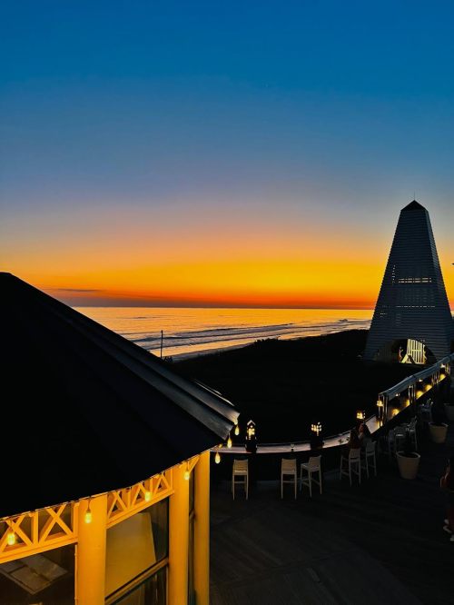 A vibrant sunset over the ocean, with a silhouette of a building and lights in the foreground.