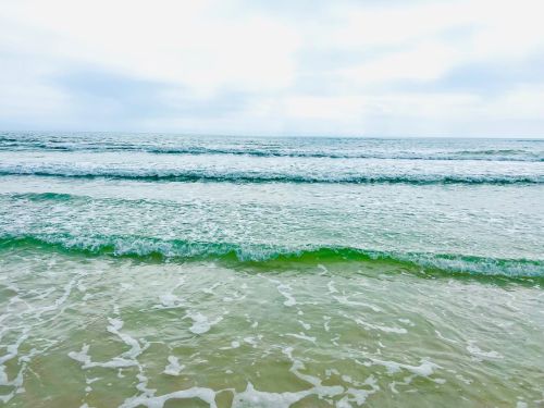 A serene view of gentle ocean waves lapping at a sandy shore under a cloudy sky.