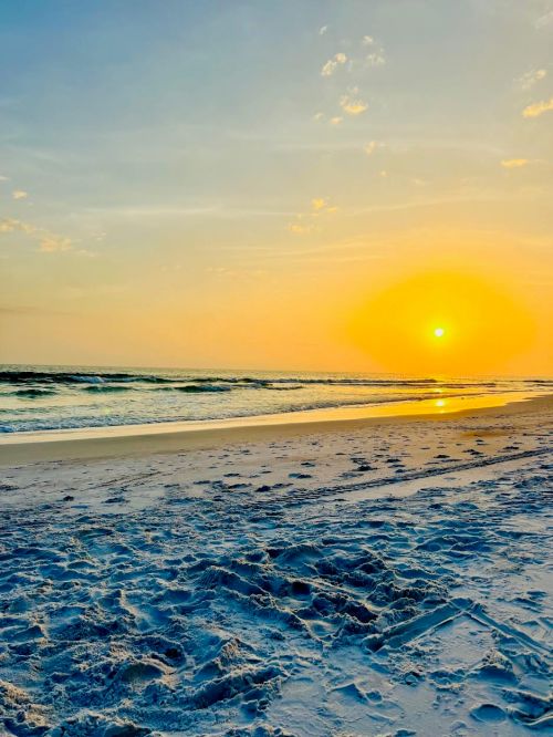 A serene beach at sunset, with golden hues reflecting on the water and soft sand in the foreground.