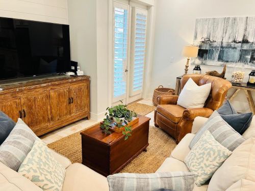 Cozy living room with a TV, wooden furniture, a leather armchair, and decorative pillows, featuring a plant centerpiece.