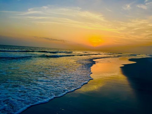 A serene beach at sunset, with gentle waves lapping at the shore and a colorful sky reflecting on the water.