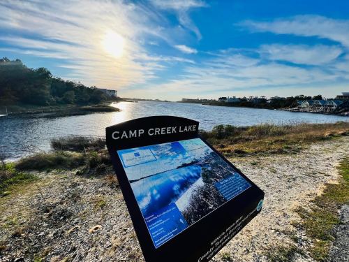 Sign for Camp Creek Lake with a scenic view of the lake and sky at sunset.