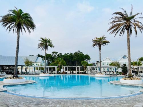A serene pool surrounded by palm trees and cozy buildings under a cloudy sky.