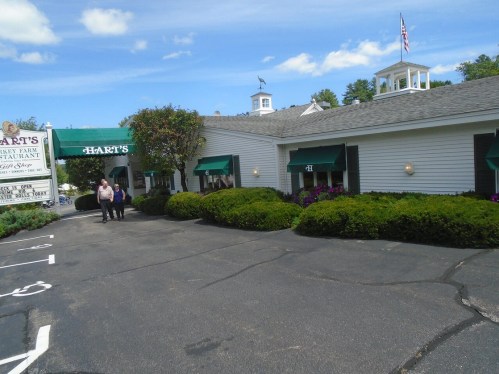 Exterior of Hart's restaurant with green awnings, shrubs, and a clear blue sky. Two people walk towards the entrance.