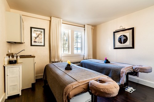 A serene massage room with two treatment tables, soft lighting, and a window overlooking nature.