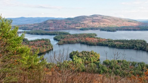 A scenic view of a lake surrounded by forested hills and colorful autumn foliage.