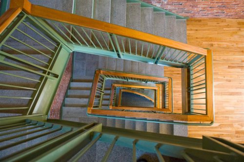 Aerial view of a spiral staircase with green railings and wooden flooring, showcasing a geometric pattern.