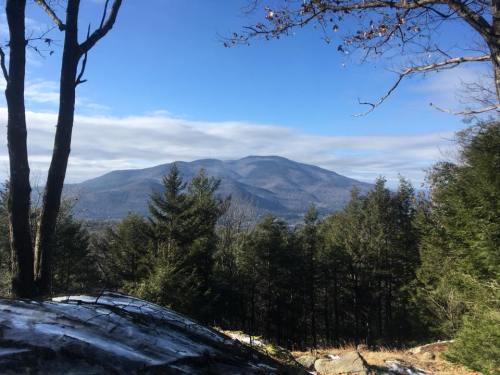 A scenic view of a mountain surrounded by trees under a clear blue sky, with some snow on the ground.