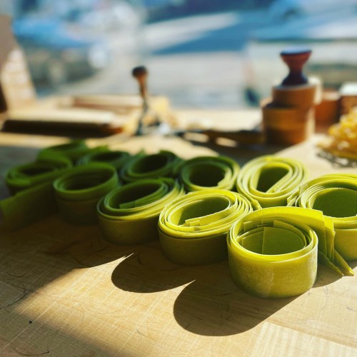 Freshly rolled green pasta laid out on a wooden surface, with soft sunlight illuminating the scene.