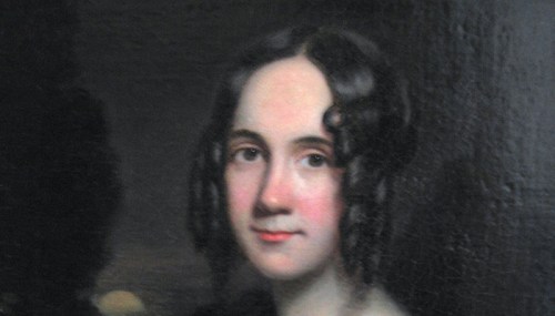Portrait of a young woman with curly hair, softly smiling against a dark background.