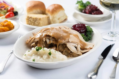 A plate of turkey with gravy, stuffing, and mashed potatoes, accompanied by rolls, salad, and a glass of wine.