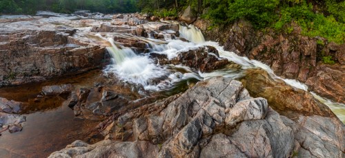 A serene river cascades over rocky terrain, surrounded by lush greenery and smooth water flowing gently.