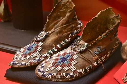 Traditional beaded moccasins displayed on a black cloth, showcasing intricate patterns and craftsmanship.