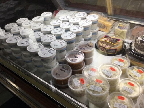 A display case filled with various containers of food, labeled with prices, including dips and side dishes.