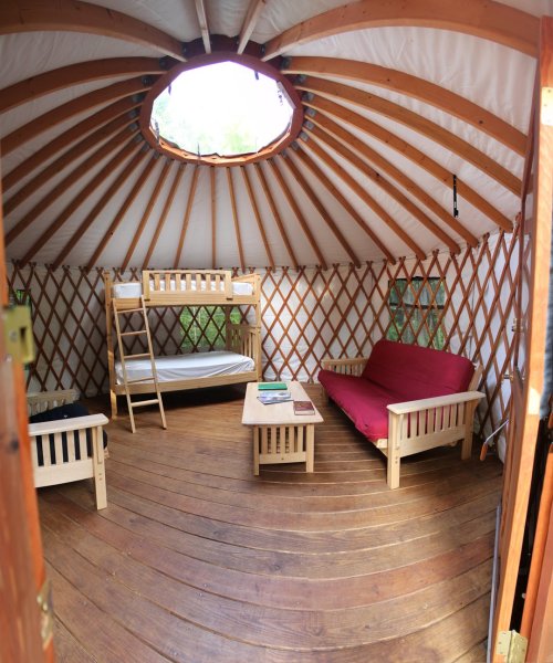 Interior of a cozy yurt with wooden furniture, a bunk bed, and a circular skylight.