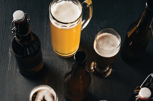 A variety of beer bottles and glasses on a dark wooden surface, featuring different types of beer.