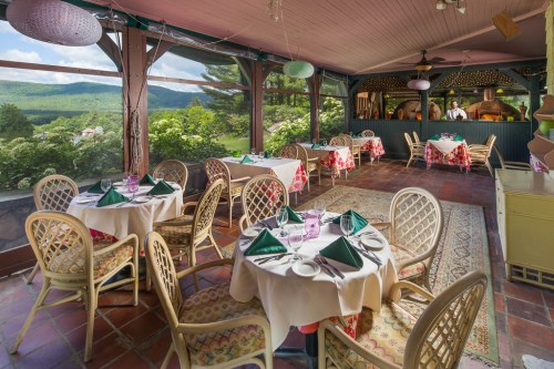 A cozy dining area with round tables, green napkins, and a scenic view of mountains through large windows.