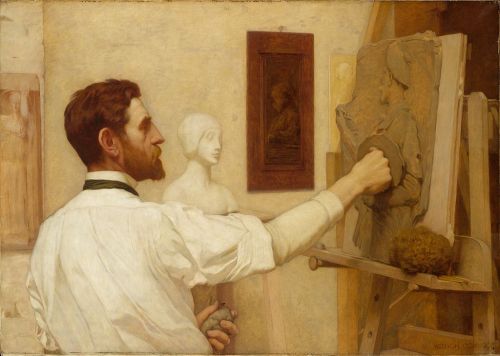 A male artist sculpts a figure from stone, with a bust and painting visible in the background.
