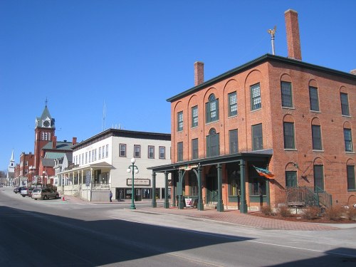 Historic buildings line a quiet street under a clear blue sky, showcasing brick architecture and a charming small-town vibe.