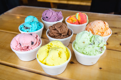 Eight cups of colorful ice cream in various flavors arranged on a wooden table.