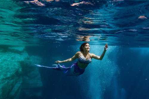 A mermaid swims gracefully underwater, surrounded by shimmering blue water and light.