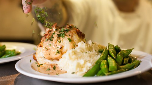 A plate of salmon topped with herbs, served with mashed potatoes and green snap peas.