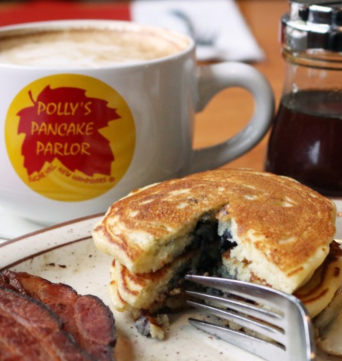 A plate with blueberry pancakes, bacon, and a cup of coffee from Polly's Pancake Parlor, with syrup on the side.