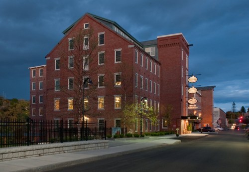 Historic brick building at dusk, featuring large windows and a welcoming entrance, with streetlights illuminating the scene.