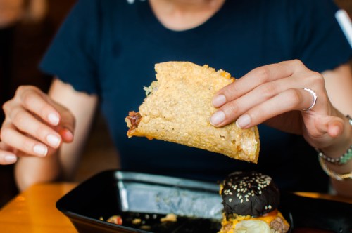 A person holds a taco above a plate with a black burger, ready to take a bite.