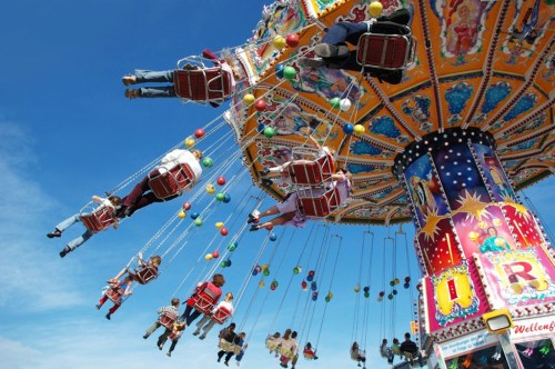 A colorful swing ride with people enjoying the view against a bright blue sky.