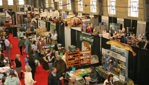 A bustling trade show with vendors, displays, and crowds in a large indoor space.