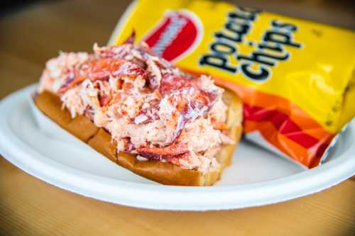 A lobster roll filled with lobster meat on a bun, served with a side of potato chips.