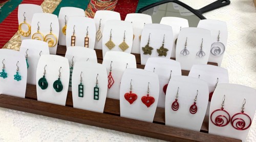 A display of colorful earrings in various shapes and designs, arranged on white cards in a wooden holder.