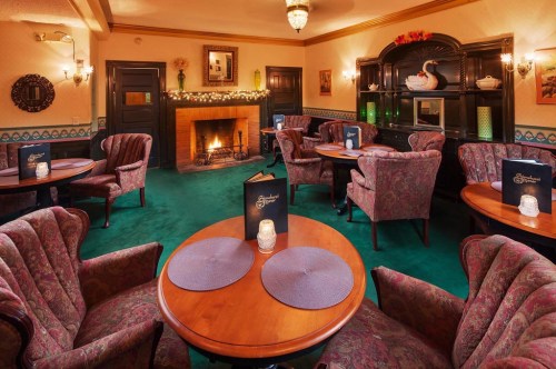 Cozy lounge with plush chairs, wooden tables, and a fireplace, decorated for a warm, inviting atmosphere.