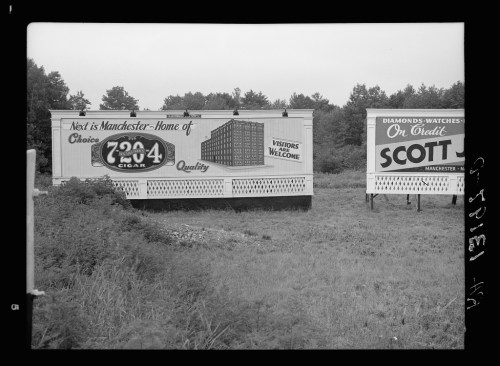 Two vintage billboards in a grassy area, one promoting Manchester and the other advertising Scott's watches.