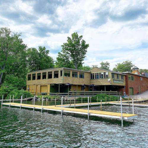 A lakeside building with a dock, surrounded by trees and a cloudy sky.