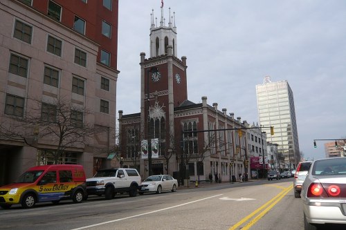 A street view featuring a historic clock tower building alongside parked cars and modern buildings in the background.