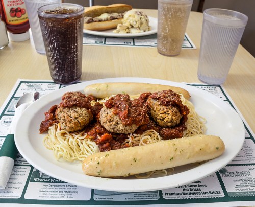 A plate of spaghetti topped with meatballs and marinara sauce, accompanied by two breadsticks and a drink.