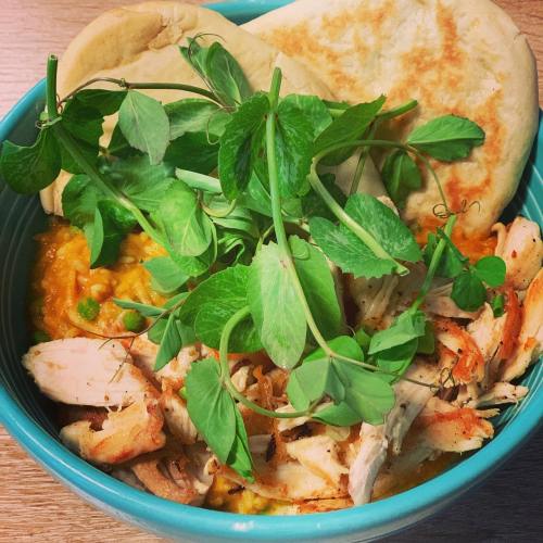 A bowl of shredded chicken, orange puree, peas, and fresh greens, accompanied by two flatbreads.