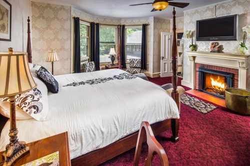 Cozy bedroom with a four-poster bed, fireplace, and elegant decor, featuring a warm ambiance and large windows.