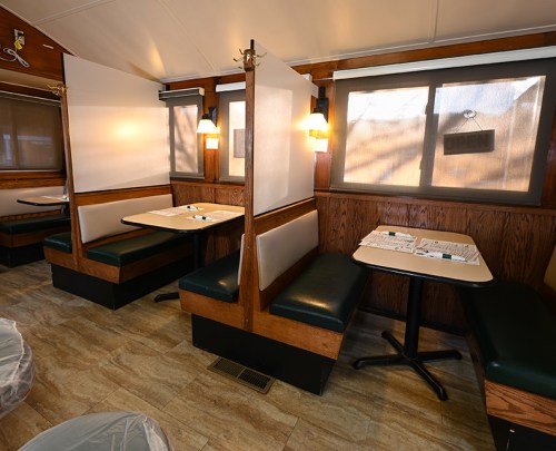 Interior of a restaurant with booths, partitions, and large windows, featuring a warm, inviting atmosphere.