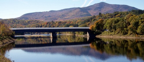 A serene river scene with a bridge, surrounded by colorful autumn foliage and mountains in the background.