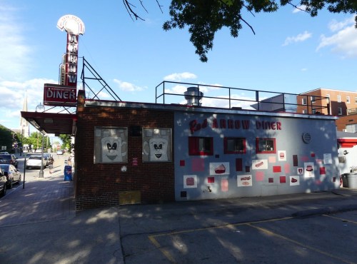 A retro diner with a brick exterior, featuring cartoonish faces on the windows and a sign reading "Red Arrow Diner."