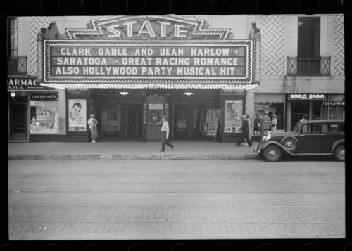 Historic theater marquee advertising "Saratoga" with Clark Gable and Jean Harlow, featuring vintage cars and pedestrians.