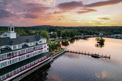 A scenic view of a lakeside hotel at sunset, with a dock and lush greenery surrounding the calm water.